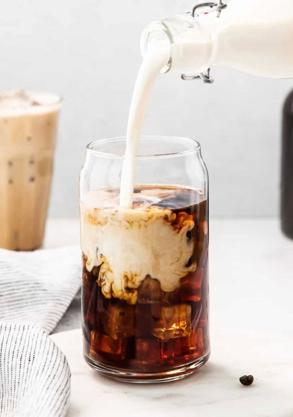 An iced coffee being poured into a glass.