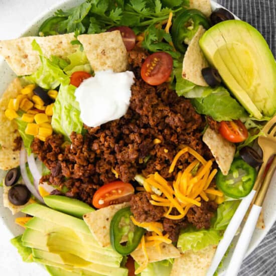 Mexican taco salad in a white bowl with sour cream and guacamole.