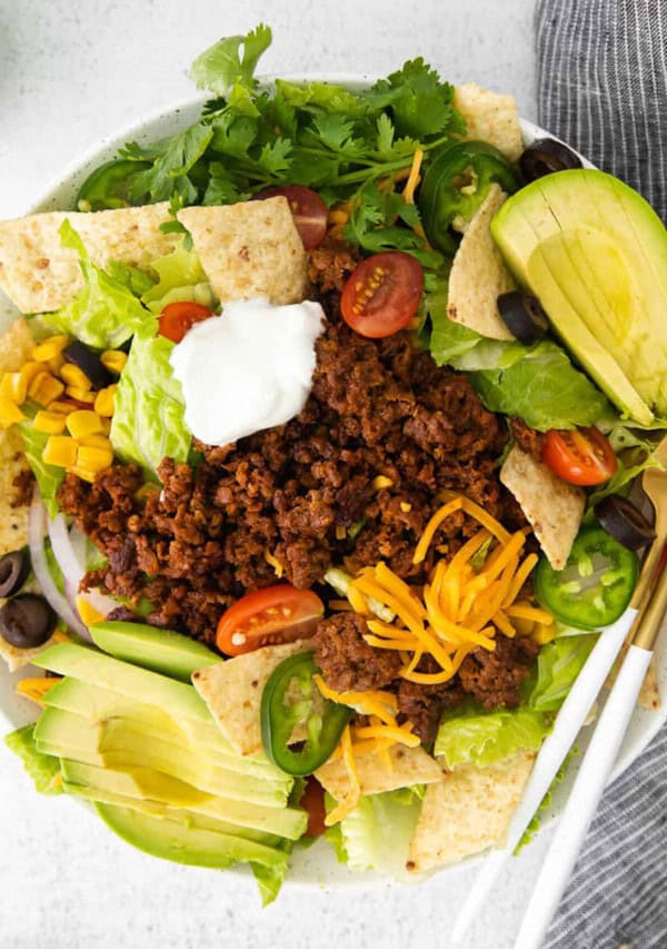 Mexican taco salad in a white bowl with sour cream and guacamole.