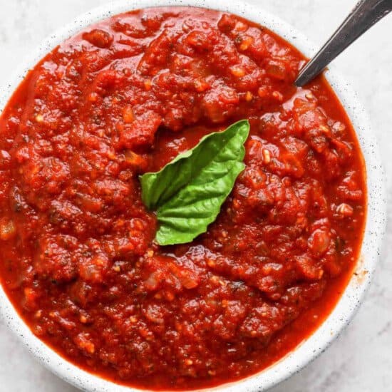 A bowl of tomato sauce with a basil leaf.