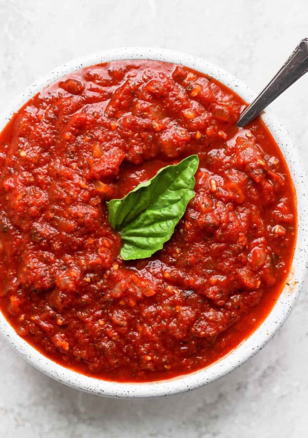 A bowl of tomato sauce with a basil leaf.