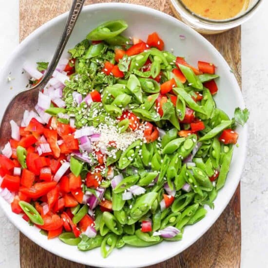 A bowl of salad with greens, tomatoes, and dressing on a wooden cutting board.
