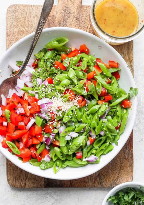 A bowl of salad with greens, tomatoes, and dressing on a wooden cutting board.