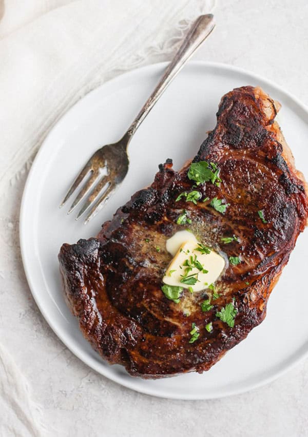 A steak on a plate with butter and herbs.