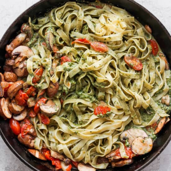 Pesto pasta in a skillet with mushrooms and tomatoes.
