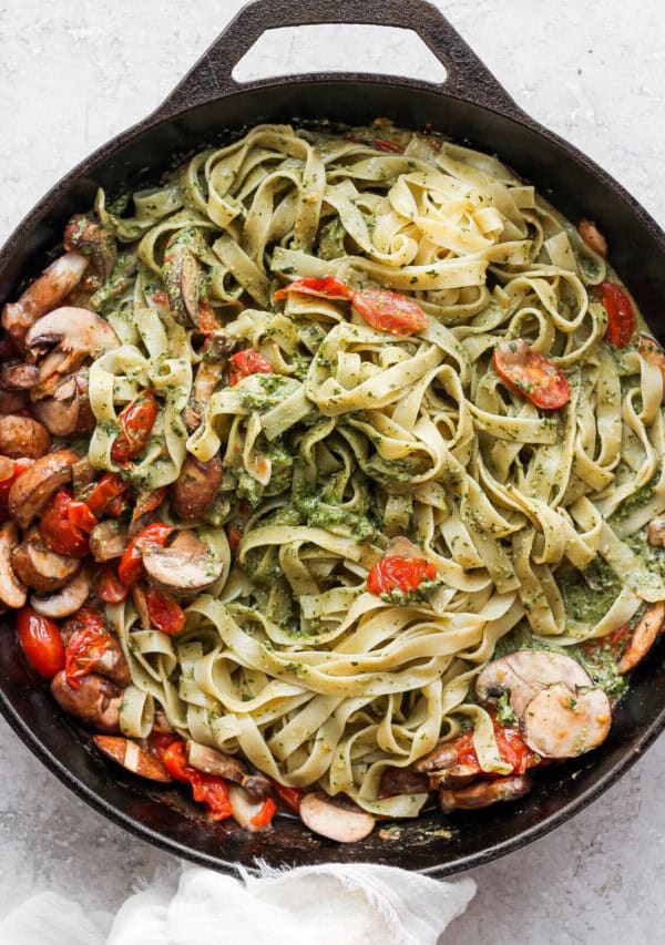 Pesto pasta in a skillet with mushrooms and tomatoes.