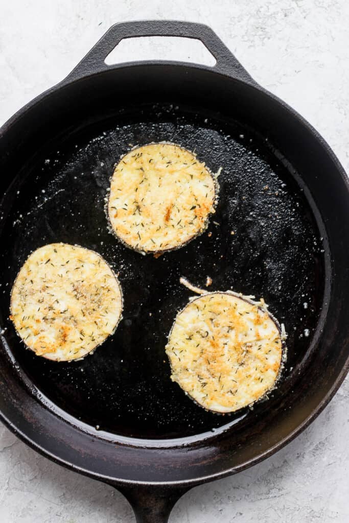 Browning eggplant rounds in a skillet pan. 
