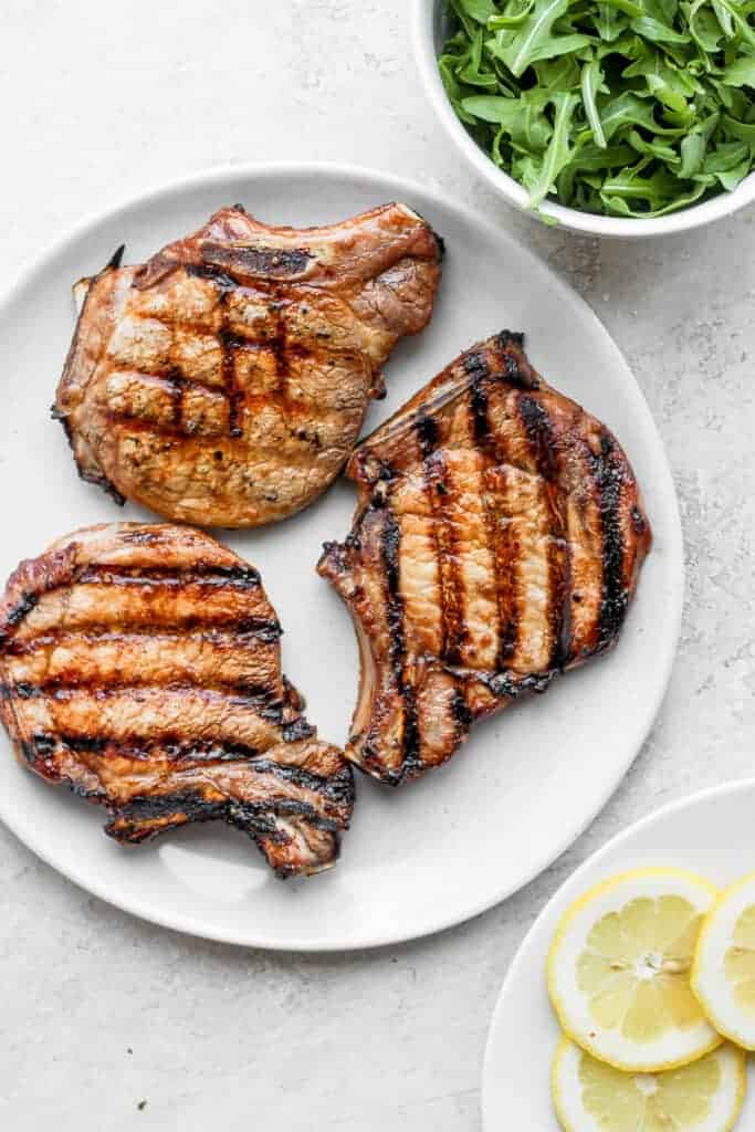 grilled pork chops on plate next to arugula