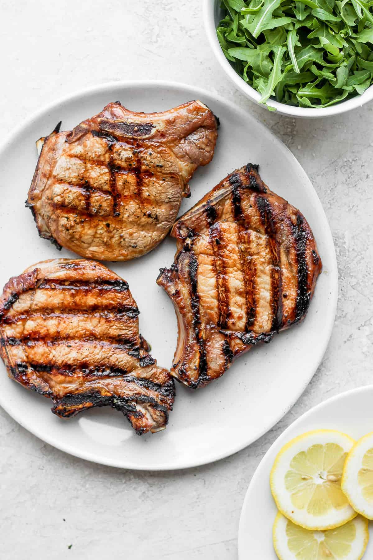 grilled pork chops on plate next to arugula.