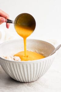 a person pouring orange juice onto peach muffins.