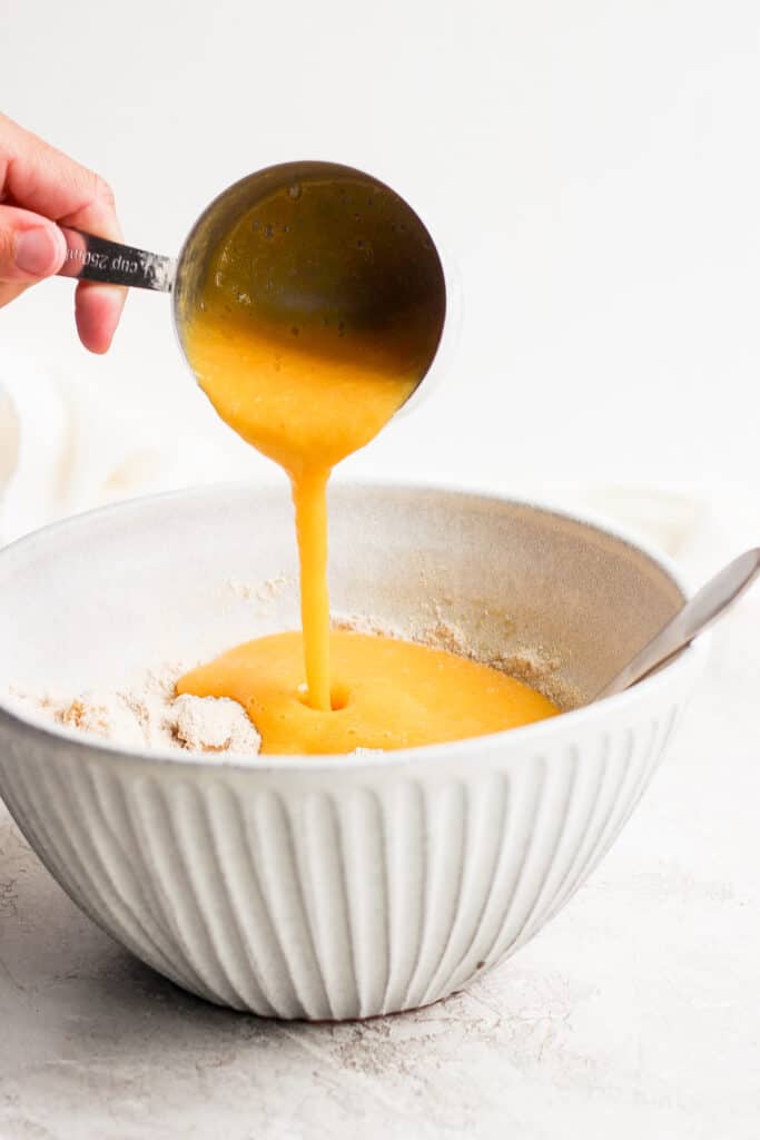 pureed peaches being poured in a bowl with the rest of the peach muffin ingredients