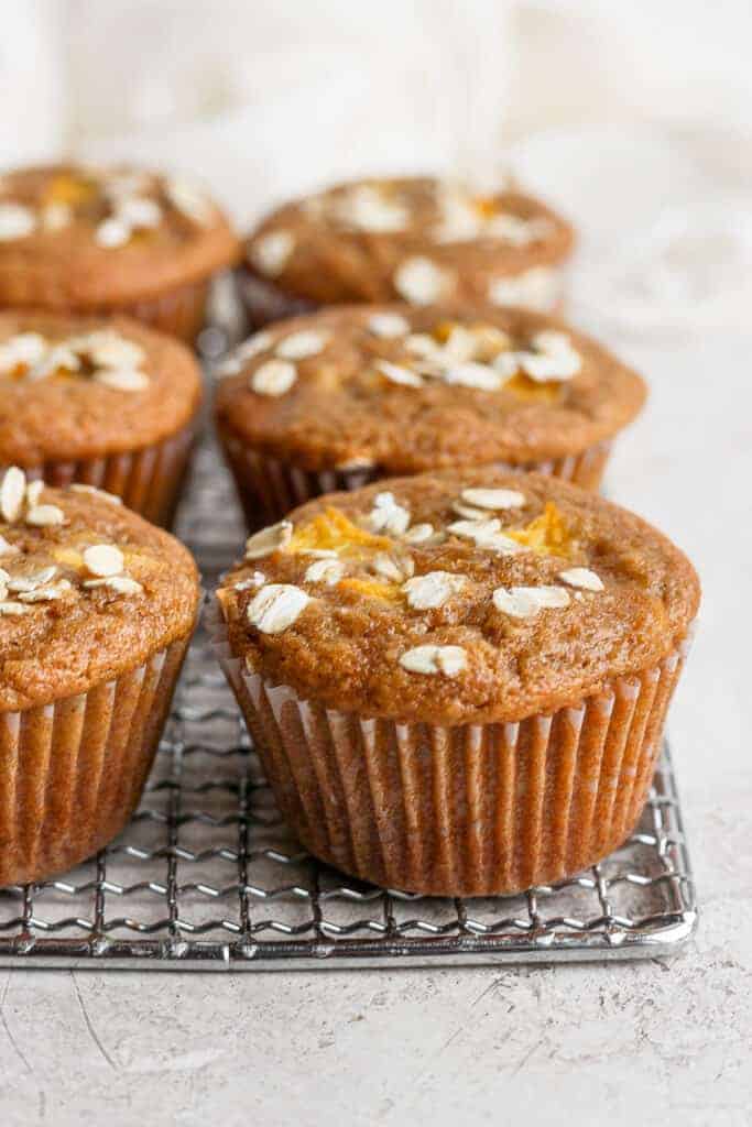 peach muffins on a cooling rack topped with rolled oats