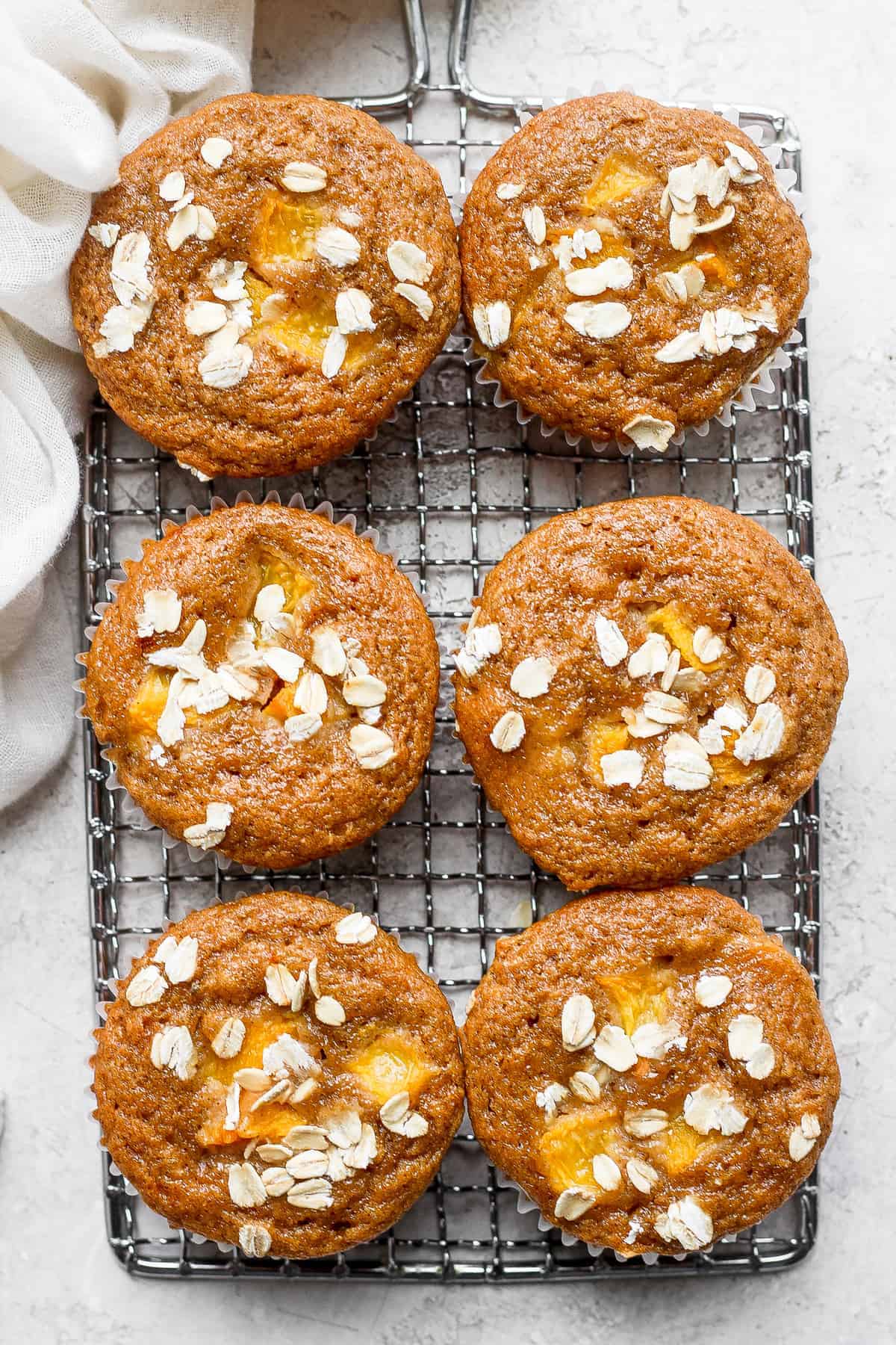 peach muffins on a cooling rack topped with rolled oats