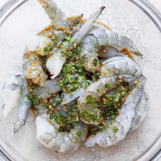 Grilled prawns in a glass bowl with herbs, marinade.