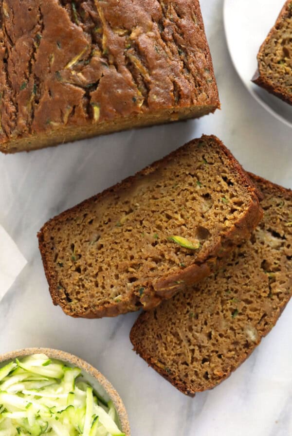 slices of zucchini bread next to a bowl of zucchini.