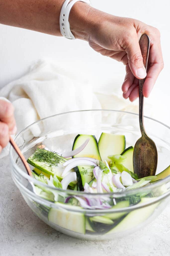 tossing zucchini salad ingredients together with spoons