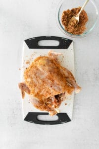 A Beer Can Chicken seasoned with spices, sitting on a cutting board.