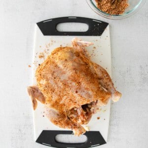 A Beer Can Chicken seasoned with spices, sitting on a cutting board.