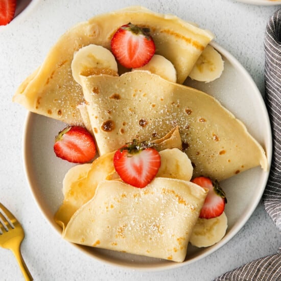 Crepes on a plate topping with strawberries and bananas.