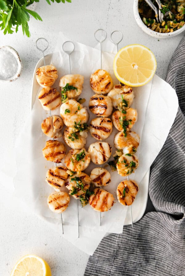 Grilled scallops served on skewers with lemon wedges.