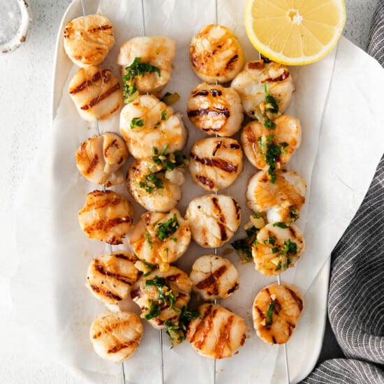 Grilled scallops skewers with lemon wedges.