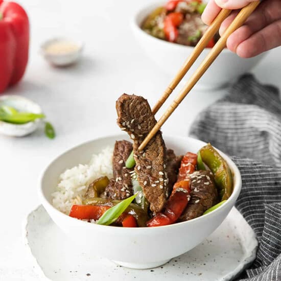 beef stir fry in a white bowl with chopsticks.