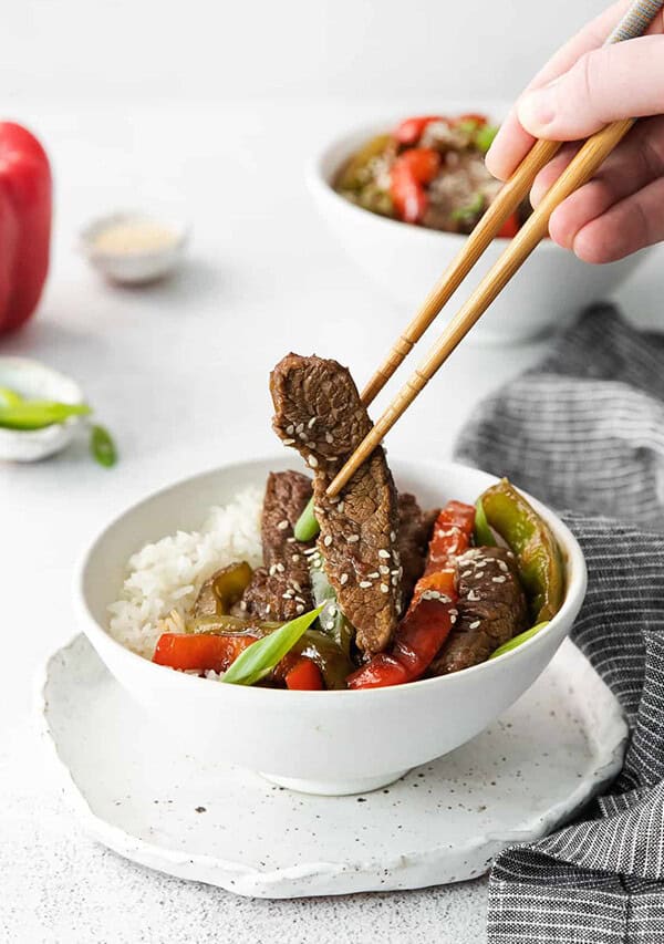 beef stir fry in a white bowl with chopsticks.