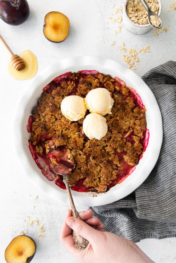 plum crumble in a white bowl with a scoop of ice cream.