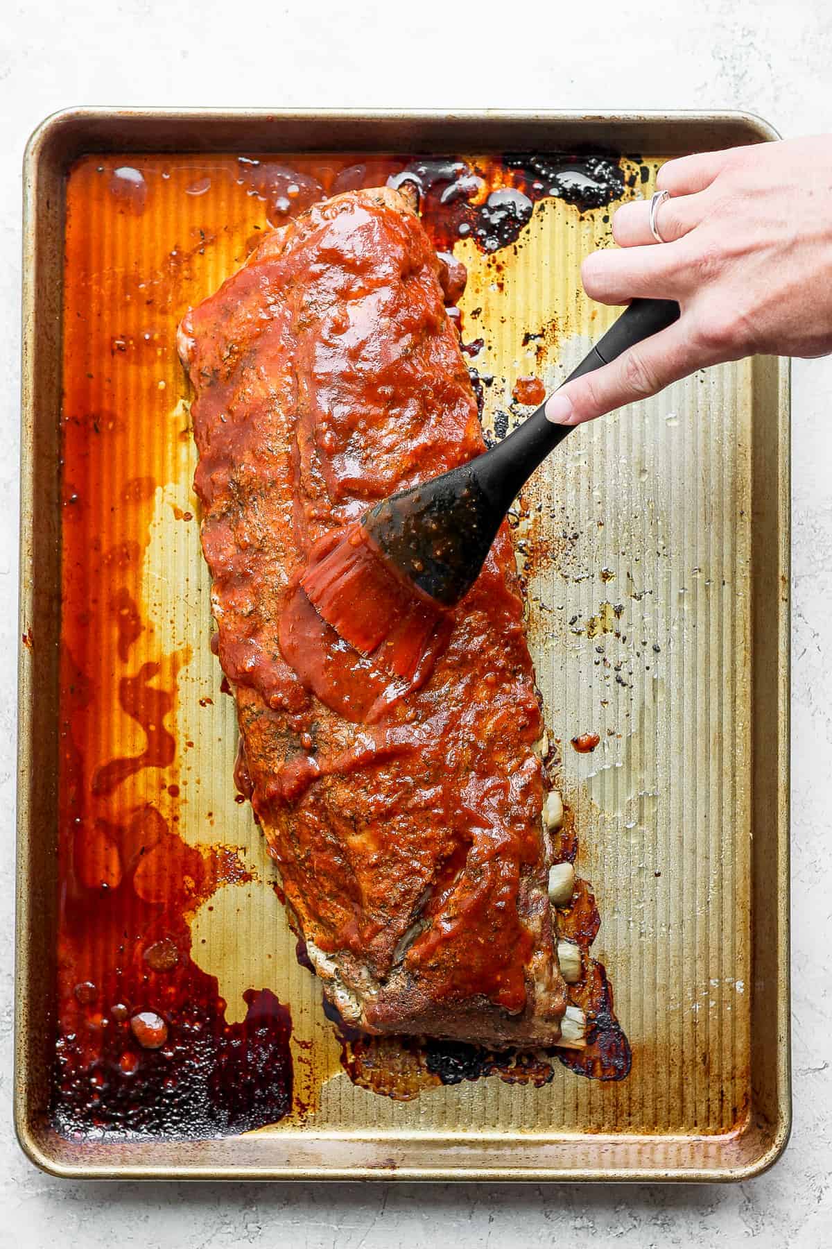 homemade BBQ sauce being used on a rack of ribs.