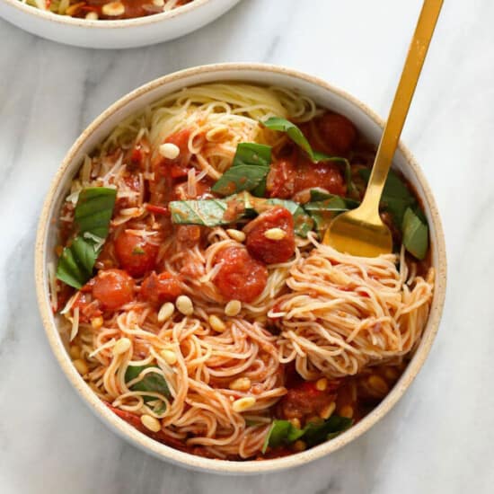 Two bowls of spaghetti with tomato sauce and pine nuts.