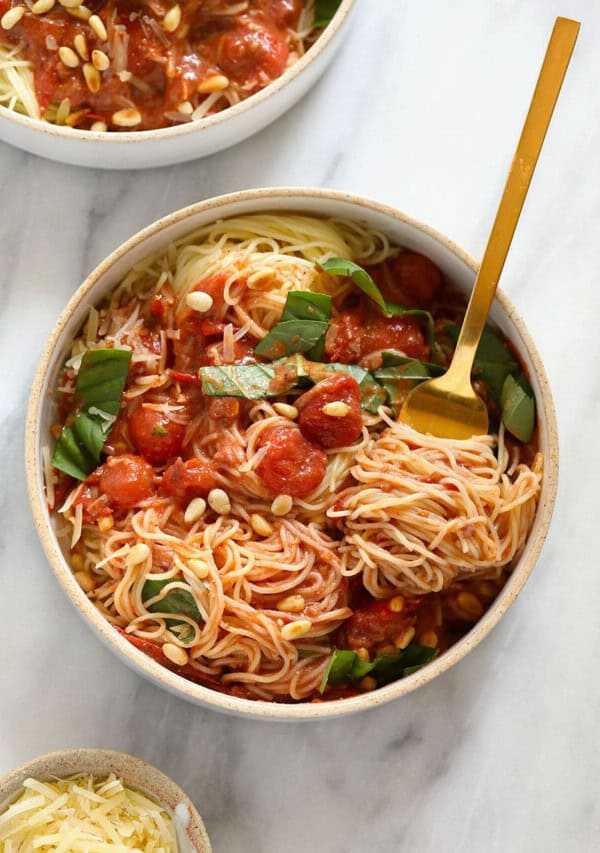 Two bowls of spaghetti with tomato sauce and pine nuts.