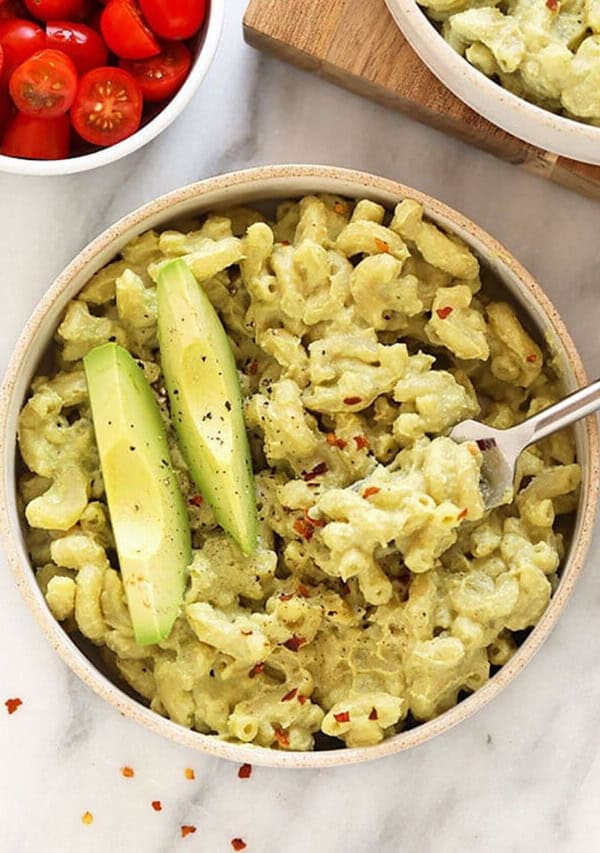 A bowl of guacamole pasta with tomatoes and avocado.