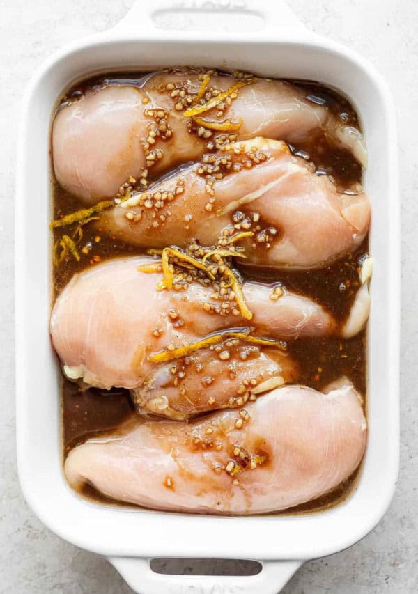 raw chicken in a white casserole dish with sesame seeds.