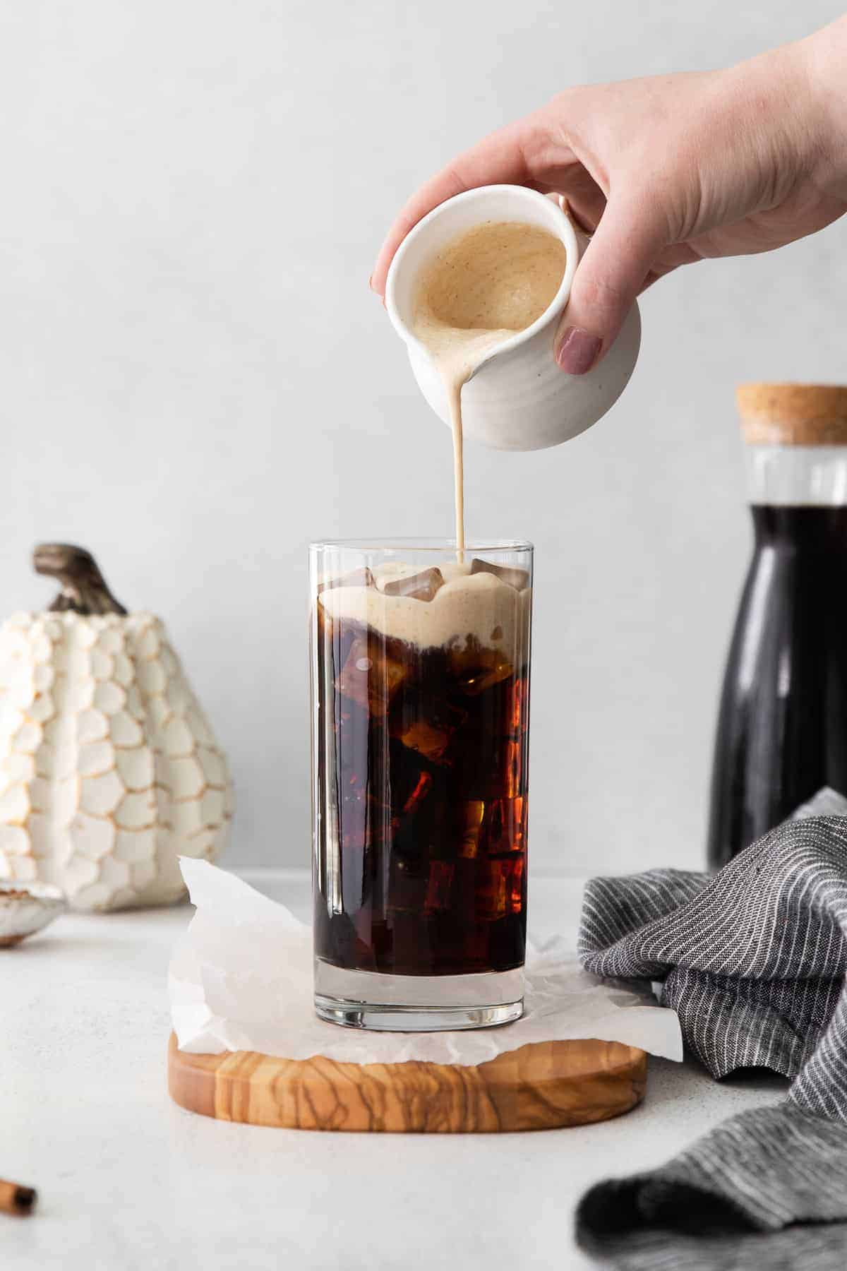 Pouring Pumpkin Cream Cold Brew over cold brew on ice. 