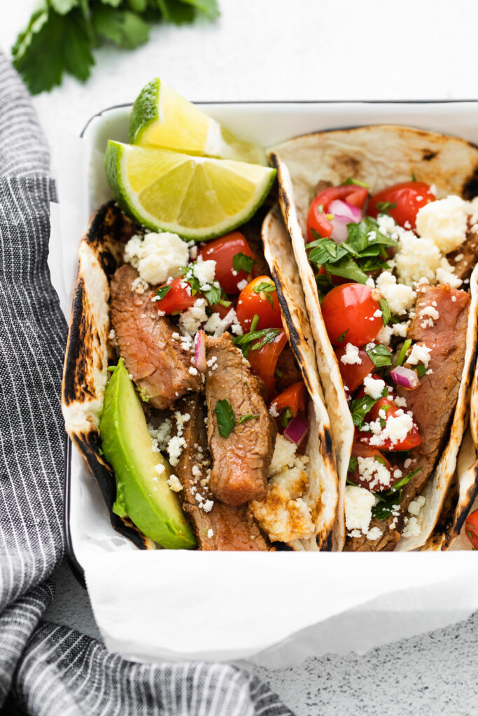 Close up photo of steak tacos garnished with fresh lime slices.