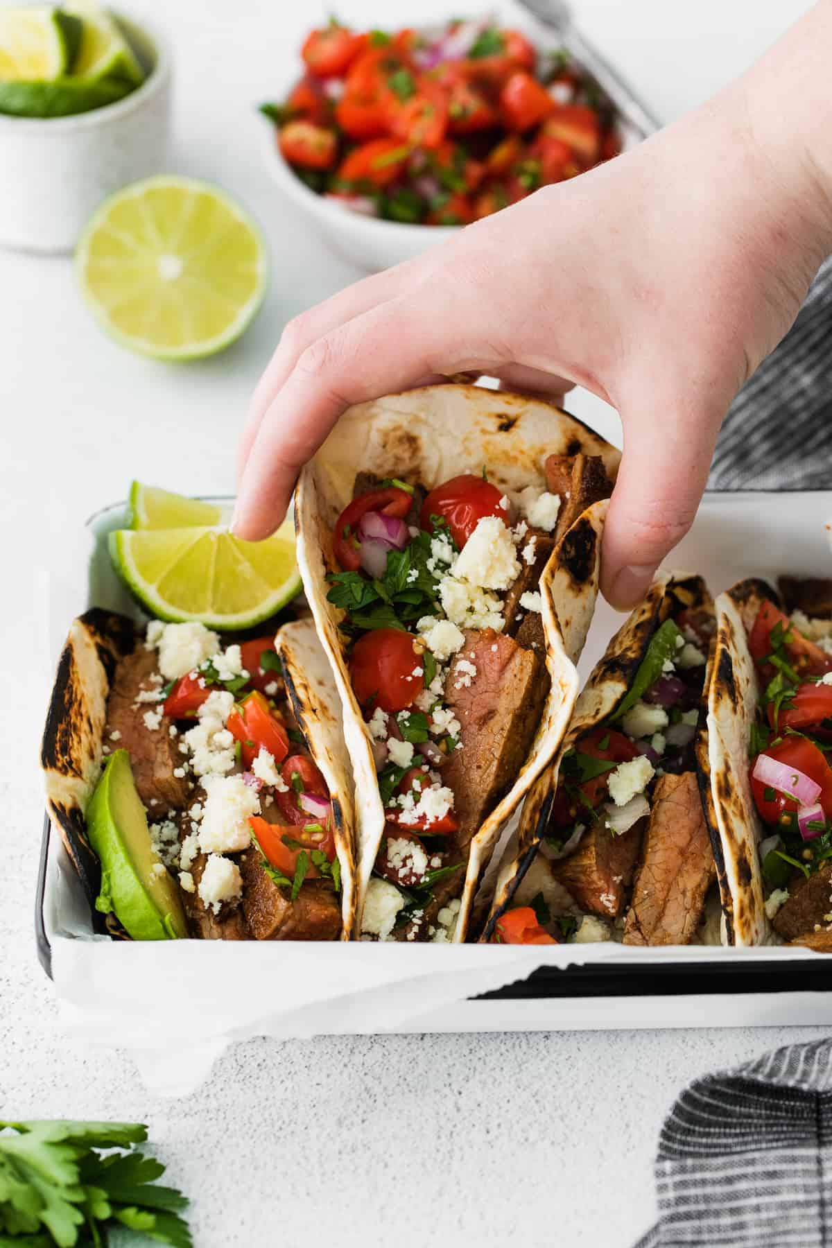 hand grabbing a steak taco from a platter of steak tacos