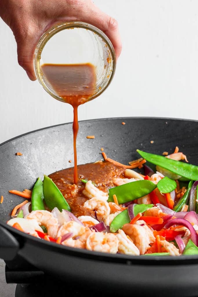 stir fry sauce being poured over a stir fry in a skillet