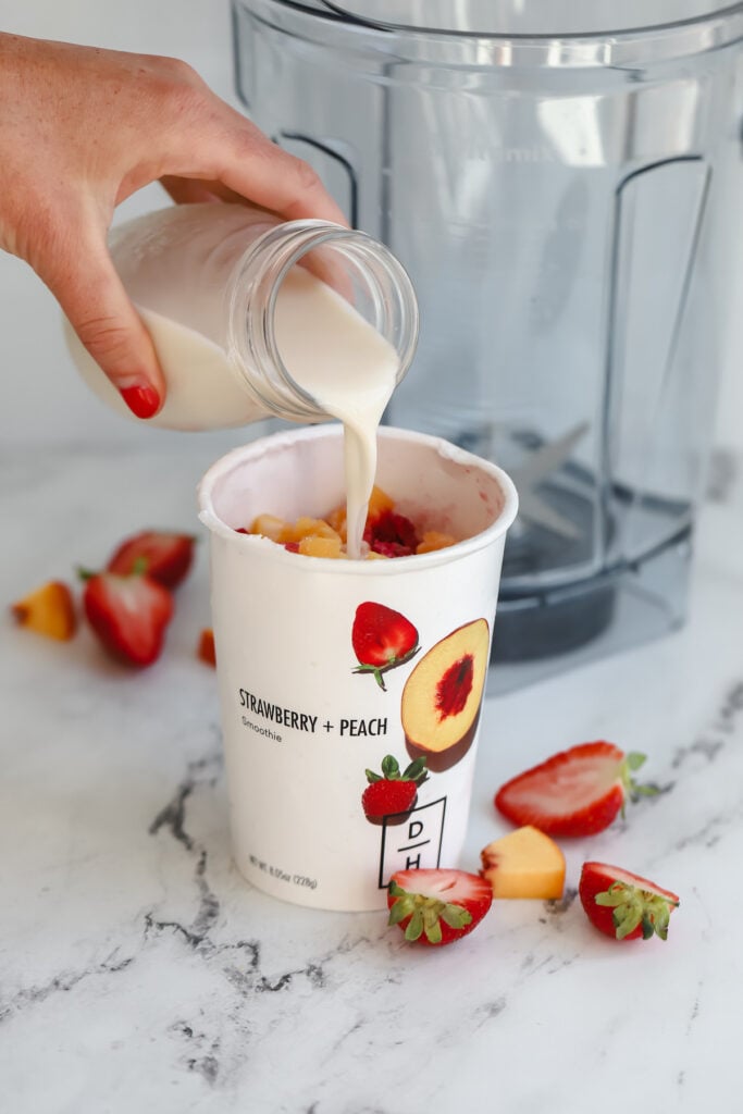 milk being poured in a smoothie cup before being put in a blender