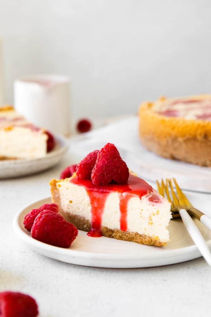 a slice of healthy cheesecake topped with raspberry swirl and additional fresh raspberries