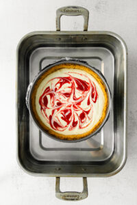 a red and white swirled Greek yogurt cheesecake in a metal pan.