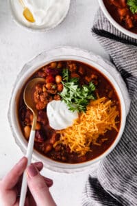 a person holding a bowl of instant pot chili with sour cream.