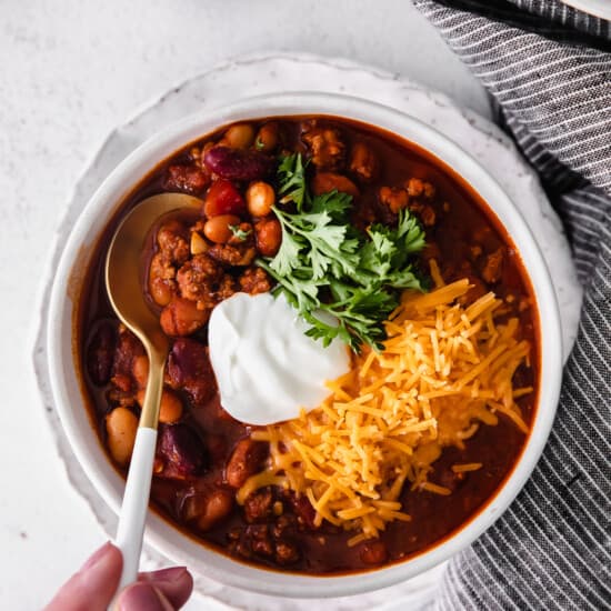 a person holding a bowl of instant pot chili with sour cream.
