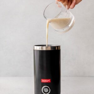 A person preparing a London Fog drink by pouring milk into a coffee maker.