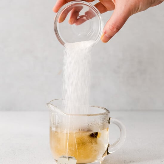 a hand is pouring sugar into a cup of London fog tea.
