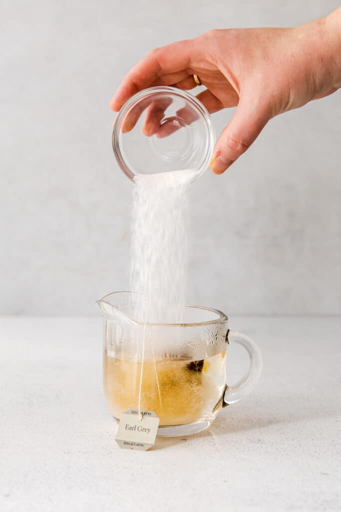 granulated sugar being poured into a mug of earl grey tea