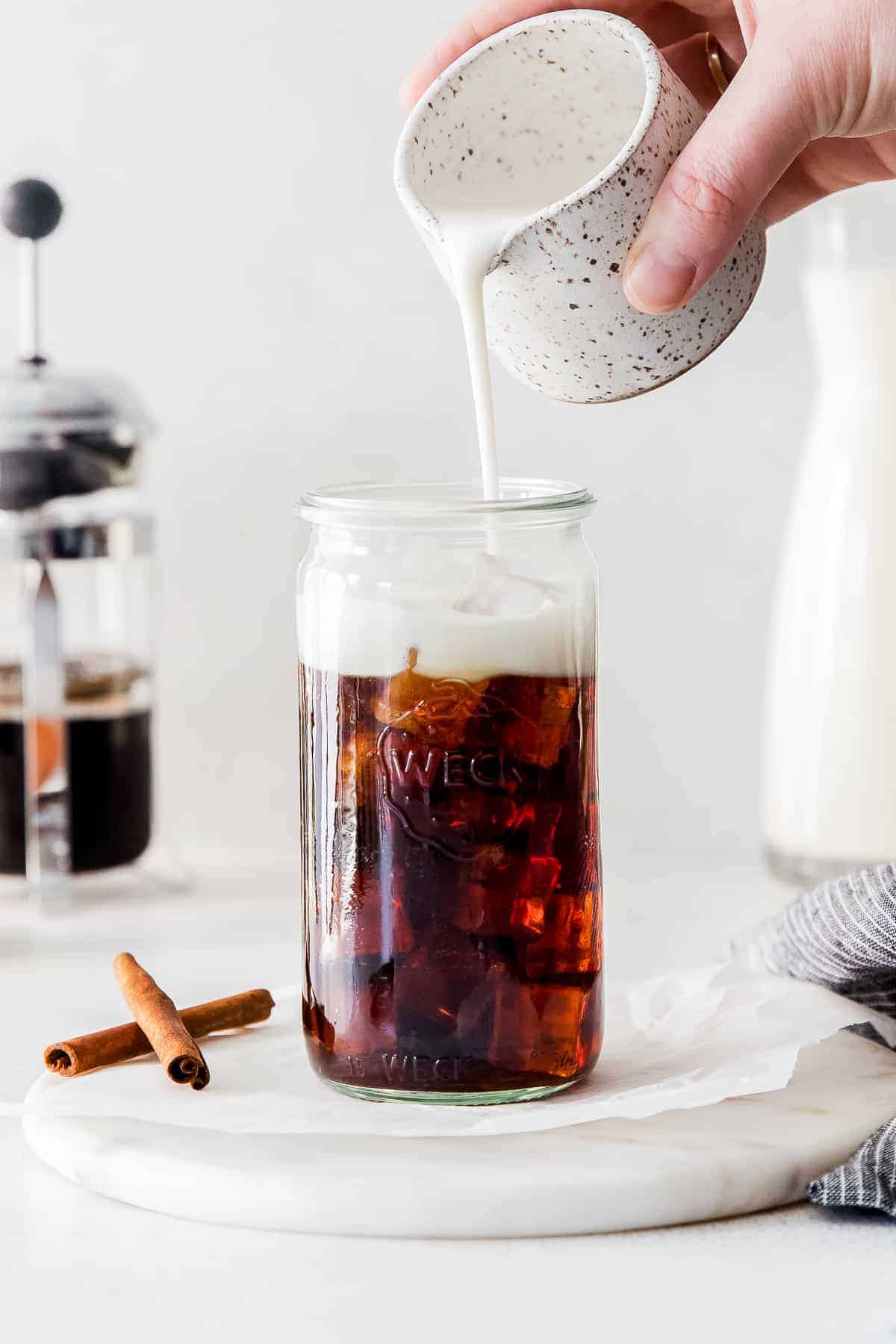 pouring oat milk in coffee glass