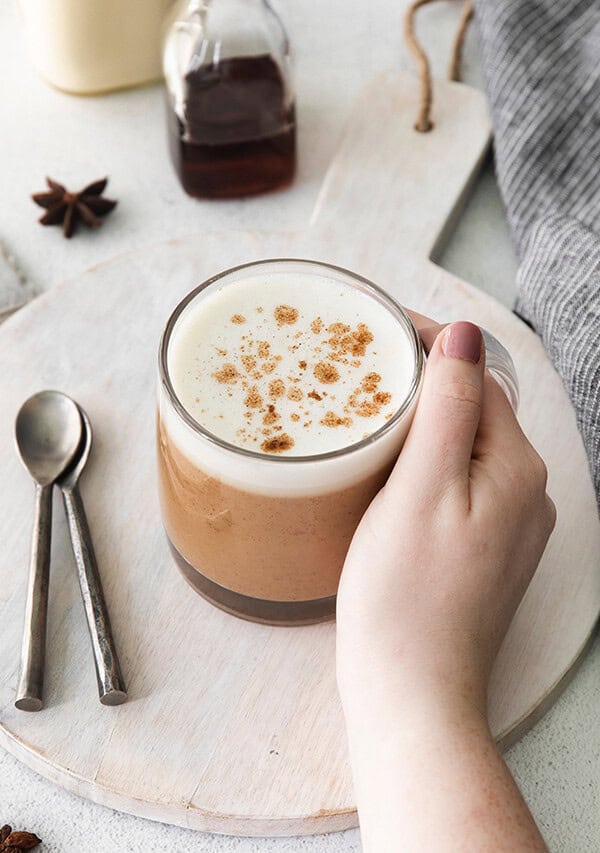 a person holding a latte with cinnamon and nutmeg on a plate.