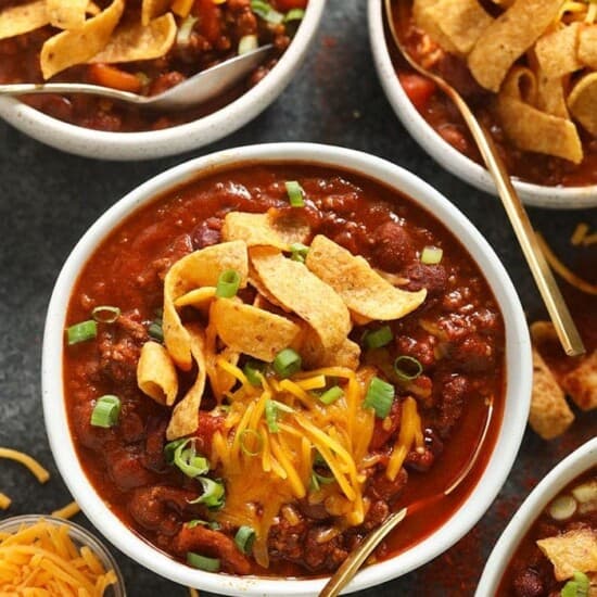 Four bowls of the best chili with cheese and tortilla chips.