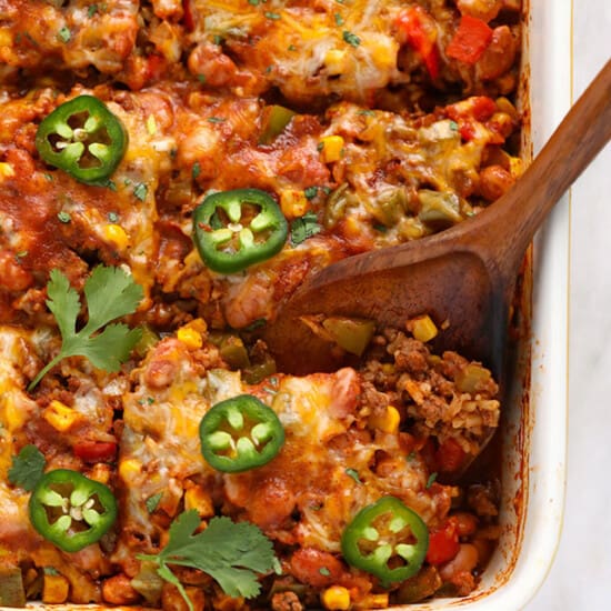 mexican lasagna in a baking dish with a wooden spoon.