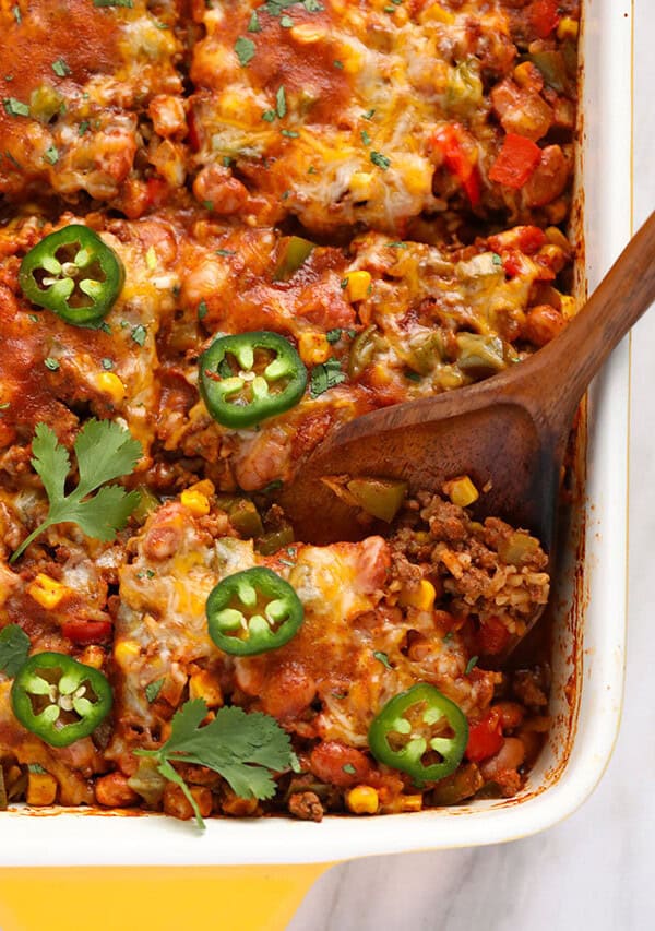 mexican lasagna in a baking dish with a wooden spoon.